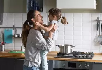 A mom holding her daughter in her arms standing in the kitchen.